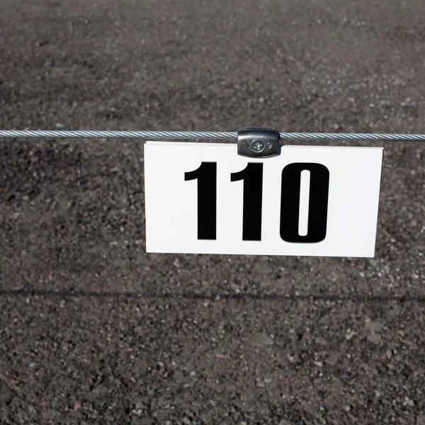 A plastic white plate with the number of a free parking space hangs on an iron cable against the background of asphalt during the day.