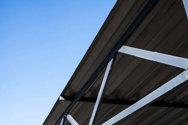 Iron structure, roof covered with corrugated aluminum sheets on metal supports, against a clear blue sky during the day.