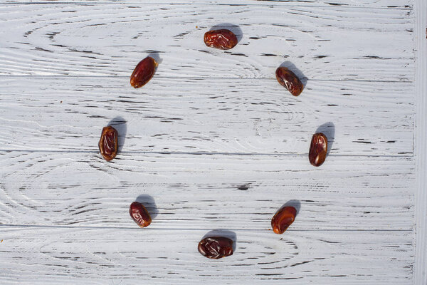 Composition of dried dates laid out in the form of a circle on a light wooden, textured surface. Creative background for your design.