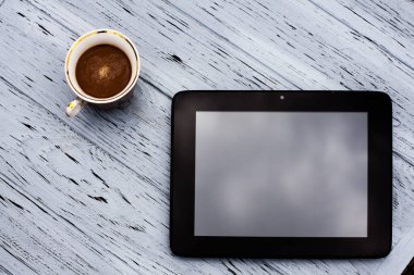 Bir bardak aromatik sade kahve ve açık ahşap bir masada siyah bir tablet..