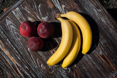 Olgun meyveler, muzlar ve iştah açıcı şeftalilerle dolu, koyu kahverengi ahşap bir masa üzerinde.