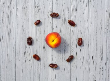 Kurumuş hurmaların bileşimi daire şeklinde dizilmiş ve şeftali, açık ahşap, desenli bir yüzey üzerinde. Tasarımınız için yaratıcı arkaplan.