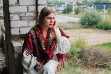 Ukrayna 'daki savaşın teması üzerine sanat çalışmaları. Ulusal elbiseli ağlayan bir Ukraynalı kadın Rus ordusu tarafından bombalanan binanın penceresinde oturuyor..