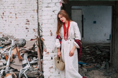 Art work on the theme of the war in Ukraine. A frustrated Ukrainian woman in national clothes and a bag in her hands stands near the ruins of a building bombed by the Russian army.