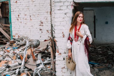 Art work on the theme of the war in Ukraine. A frustrated Ukrainian woman in national clothes and a bag in her hands stands near the ruins of a building bombed by the Russian army.