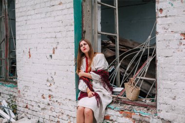 Art work on the theme of the war in Ukraine. A frustrated Ukrainian woman in national dress sits in the window frame of a building bombed by the Russian army.