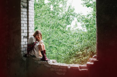 Art work on the theme of the war in Ukraine. A frustrated Ukrainian woman in national dress sits in the window frame of a building bombed by the Russian army.