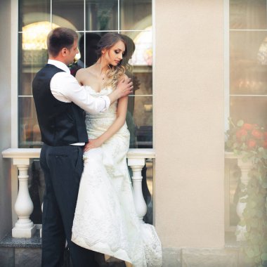 Güzel yeni evliler şık bir restoranın içinde. Beyaz gelinlikli gelin pencerede oturur, damat yanında durur ve kızı omzundan tutar..