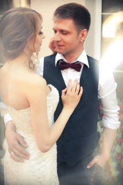 Sanat eserleri. Yeni evliler şık bir şekilde restoranın arka planına sarılıyorlar. Gelin hafif bir gelinlik giyiyor, damat beyaz gömlek, kazak ve papyon giyiyor..