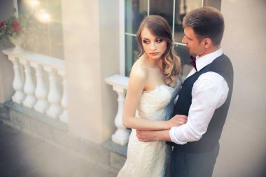 Sanat eserleri. Yeni evliler şık bir şekilde restoranın arka planına sarılıyorlar. Gelin hafif bir gelinlik giyiyor, damat beyaz gömlek, kazak ve papyon giyiyor..