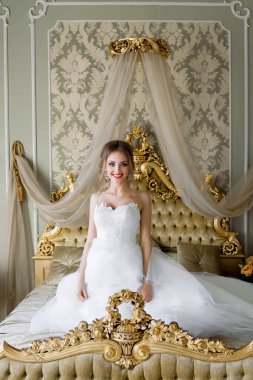 Beyaz gelinlikli güzel bir gelin, düğün öncesi sabah, şık bir iç dekorasyonu olan bir yatak odasında oturuyor..