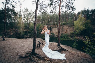 Sanat eserleri. Uzun beyaz kumaşa sarılmış zarif saç stili olan ince, güzel bir kadın gölün yukarısındaki pitoresk bir uçurumun kenarında çam ağaçlarının arasında duruyor..