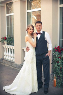 Sanat eserleri. Yeni evliler şık bir şekilde restoranın arka planına sarılıyorlar. Gelin hafif bir gelinlik giyiyor, damat beyaz gömlek, kazak ve papyon giyiyor..