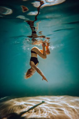Sanat eserleri. İnce, bronz tenli, atletik vücutlu, sarı saçlı, siyah iç çamaşırlı, havuzda dalıp dönen bir kız. Tasarım ve dekorasyonunuz için estetik resim.