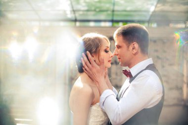 Sanat eserleri. Yeni evliler şık bir şekilde restoranın arka planına sarılıyorlar. Gelin hafif bir gelinlik giyiyor, damat beyaz gömlek, kazak ve papyon giyiyor..