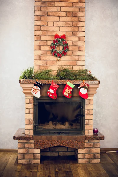 Home decorative fireplace made of bricks with candles, decorated with New Year\'s details, socks with toys, Christmas tree branches, Christmas wreath.