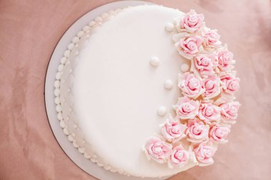 Masasında pembe çiçekler olan muhteşem bej bir doğum günü pastası..