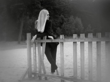 Sanat eserleri. Siyah ve beyaz bir fotoğraf, kumsalda duran, kırık ahşap bir çite dayanan sarı saçlı güzel bir kızın..