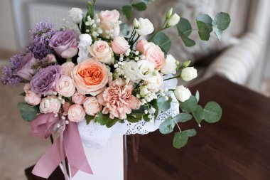 Pastel renkli güllerden yapılmış, pembe kurdelelerle süslenmiş süslü bir çiçek buketi, gün boyunca parlak bir otel odasındaki bir masanın üzerinde duruyor..