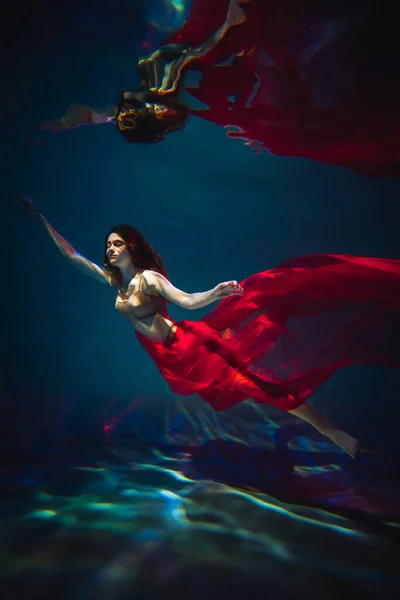 Art work. Underwater shot of a sports girl in lingerie with red material in the pool with beautiful highlights.