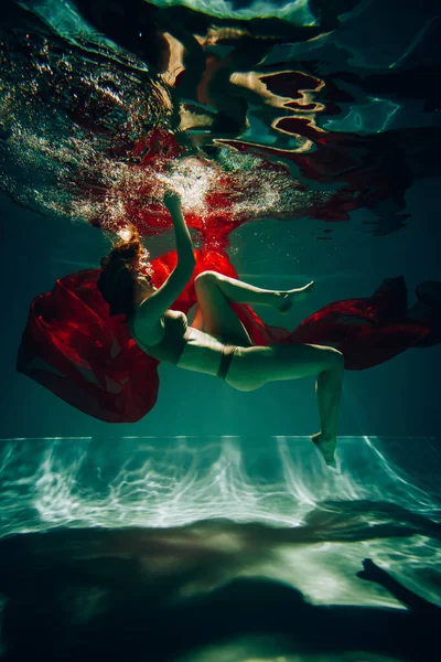 艺术品 一名身穿内衣的女运动员在水底拍摄的照片 她穿着红色的内衣 游泳池里有漂亮的亮点 — 图库照片
