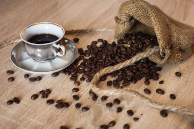 Kavrulmuş kahve çekirdekleri, küçük bir torba içinde iplerle ve kahve fincanlarıyla sabah kahvaltısı için koyu kahverengi ahşap yüzeyde içiliyor..