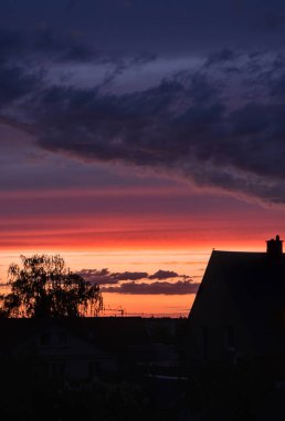 Gökyüzünde güzel bulutlar, bir evin siluetleri ve şafak vakti bir ağacın manzaralı günbatımı. 