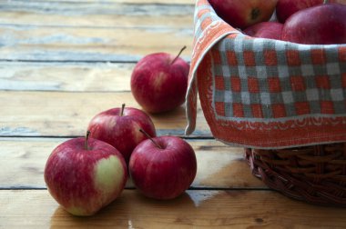 Four red apples on a wooden table. Basket of apples nearby. Napkins on the edge of the basket.