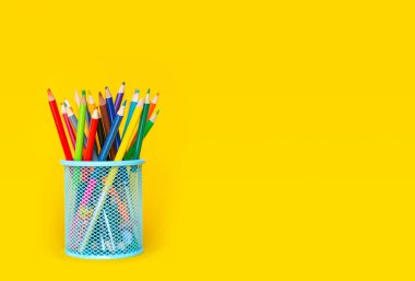 Kalemler. Sarı arka plandaki bir bardaktaki renkli kalemler.