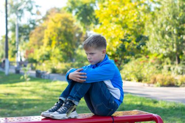 Mutsuz çocuk oturur. Sıkılmış ya da gücenmiş. Kızgın çocuk.