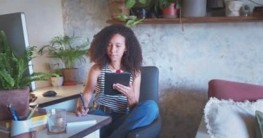 Shot of an attractive young woman sitting alone and using her tablet while working from home . High quality 4k footage