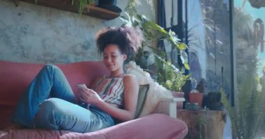 Güzel bir Afrikalı genç kadının akıllı telefonuyla evde dinlendiği bir fotoğraf. Yüksek kalite 4k görüntü