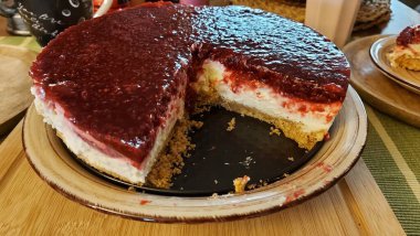 Cheesecake lezzetli bir meyve tatlısıdır. Dolgusu süzme peynir ya da mascarpone ile geliyor. Üstünde kırmızı böğürtlen reçeli var. Kırmızı tatlı reçel üstte. Meyveli kek tabakta. Yemek yakın planda..