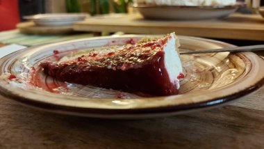 Cheesecake lezzetli bir meyve tatlısıdır. Dolgusu süzme peynir ya da mascarpone ile geliyor. Üstünde kırmızı böğürtlen reçeli var. Kırmızı tatlı reçel üstte. Meyveli kek tabakta. Yemek yakın planda..
