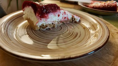 Cheesecake lezzetli bir meyve tatlısıdır. Dolgusu süzme peynir ya da mascarpone ile geliyor. Üstünde kırmızı böğürtlen reçeli var. Kırmızı tatlı reçel üstte. Meyveli kek tabakta. Yemek yakın planda..