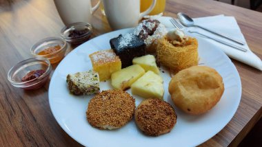 Portakal suyu. Ahşap arka planda kahve ve kek. Beyaz peçete. Kanafeh keki. Ananas dilimleri. Meyve reçelli cam kaseler. Şeker şurubu tatlısı. Kalorili kekler. Beyaz porselen tabakta tatlılar. Doğulu kurabiyeler. Hindistan cevizli çikolata küpleri.. 