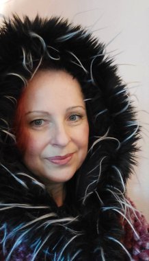 Female profile with a fur hood on her head. Winter clothes. A smiling face in close-up. Portrait with long red hair. A beautiful woman with green eyes. Winter scene. Recorded in the studio. A young adult woman.