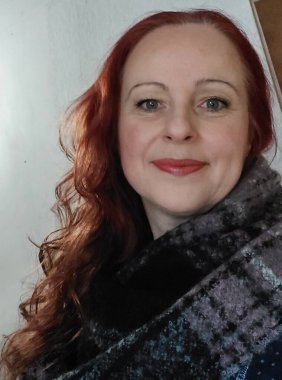 Female profile with a scarf around her neck. Winter clothes. A smiling face in close-up. Portrait with long red hair. A beautiful woman with green eyes. Winter scene. Shot in nature. A young adult.