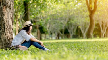Genç bir kadın çimenlerde oturuyor ve kitap okumaktan rahatlıyor.
