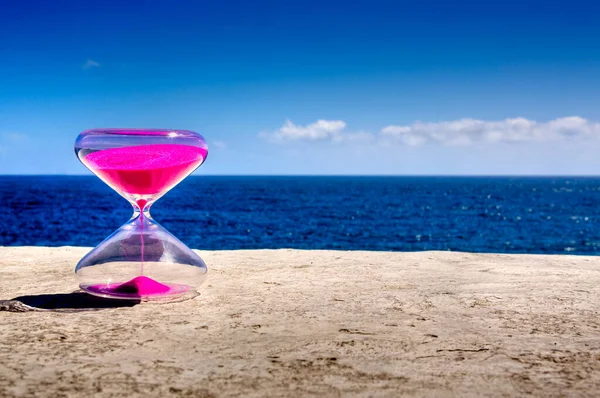 transparent glass clock of pink sand in outdoor background sky sea and land