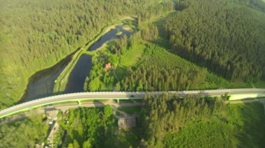 Güneşli bir yaz gününde göl ve ormanların arasında yol ve köprü üzerindeki drone 'dan görüntü.