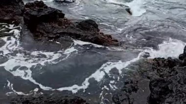 Terceira adasının güneşli havasında, taşların üzerinde dalgalar kırılır.