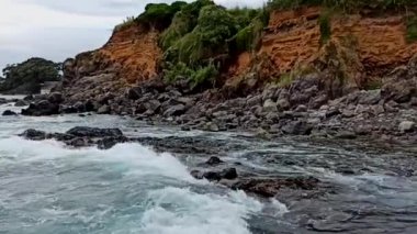 Terceira adasının güneşli havasında, taşların üzerinde dalgalar kırılır.