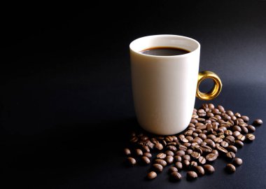 Yeni sabah aromatik ve ferahlatıcı kahvesine hoş geldiniz. Siyah arka planda beyaz kahve fincanı. Yere yığılmış kahverengi kahve çekirdekleri vardı.. 