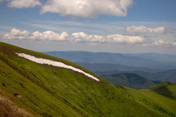 Dağ geçidinden yeşil orman vadisine kadar uzanan manzaralı bir manzara. Değişken havada ufuktaki dağ sıraları ve tepeler arasında. Kümülüs bulutlarının altında mavi gökyüzünde güneşli dağları olan yeşil bir manzara..