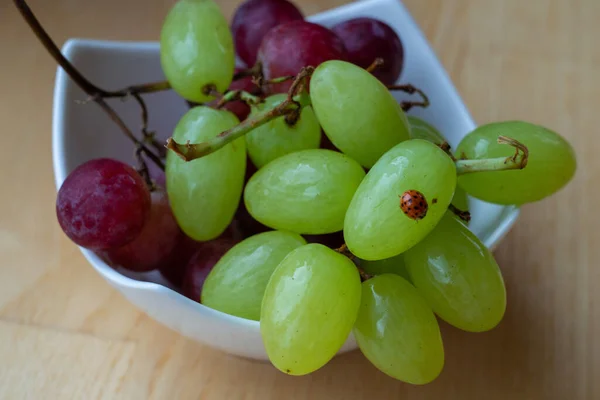 white cup of green and red grapes with little red ladybug