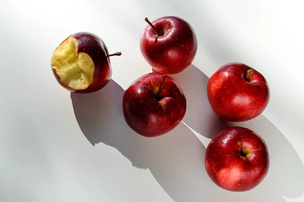 Five red ripe apples lying on a white table and their shadows