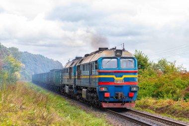 Güçlü bir mavi lokomotif, tren istasyonuna kömürlü uzun bir yük treni çeker. Demiryolu taşımacılığı.