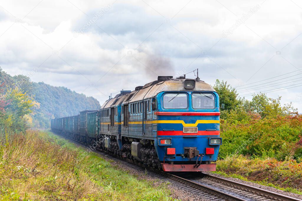 A powerful blue locomotive pulls a long freight train with coal to the railway station. Railway transportation of goods.