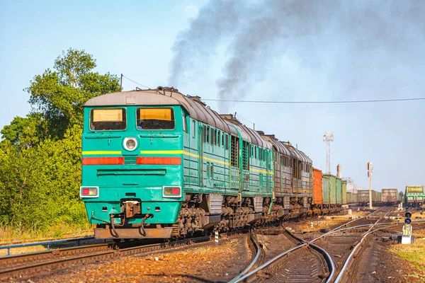 Uzun bir yük treni taşıyan dört yeşil dizel lokomotif marshalling tren istasyonundan ayrılıyor. Demiryolu taşımacılığı. Gün batımı aydınlatma.